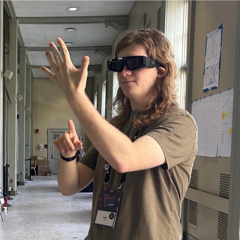 Jake Farr at MIT Reality Hack, wearing Snap Spectacles. He is holding his hand up and looking at it.